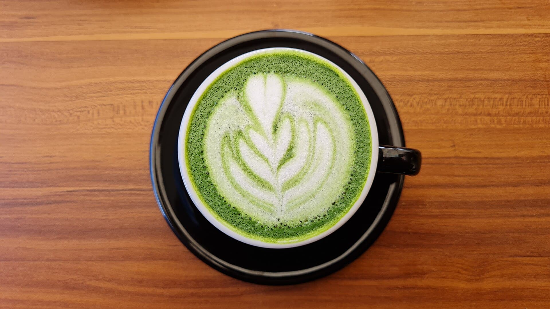 A matcha latte with a rosetta in a black cup, from above